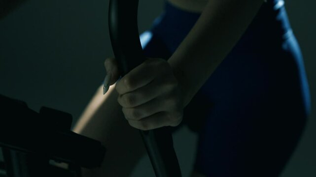 Zblizenie na kobieca dłon trzymajacą kierownice roweru stacjonarnego na silowni w czasie intensywnego treningu 