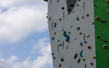 Climbing wall with overhang and colorful holds, set against blue sky. Outdoor extreme sports scene