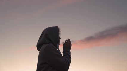 Girl praying on a pink sky background, believe in good good, ask for help, dream looking up,...