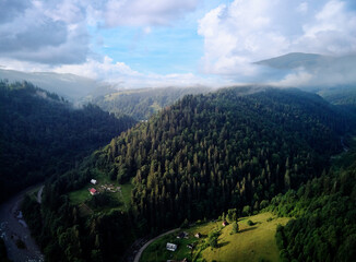 Aerial view of a lush green valley with a river flowing through, surrounded by forested mountains...