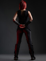 A rear view of a woman with crimson hair wearing a black outfit in a dimly lit environment. Stylish...