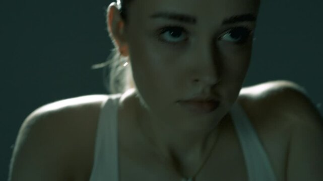 Młoda atrakcyjna kobieta w czasie wysiłku fizuycznego na rowerze streningowym w ciemnej sali z oswietleniem filmowym 