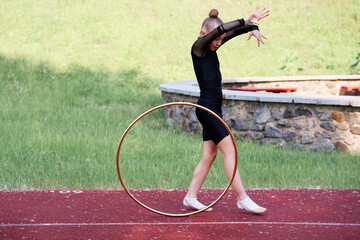 Young girl gymnast dressed in black demonstrates rhythmic gymnastics with a hoop on a track...
