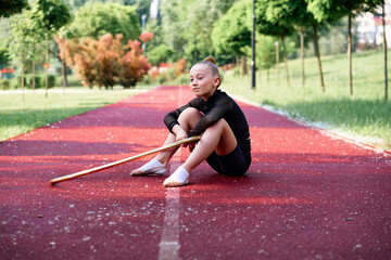 A young gymnast in a sporty outfit sits on a running track holding a hoop, demonstrating focus and grace. Young Gymnast Resting with a Hoola Hoop on Outdoor Track