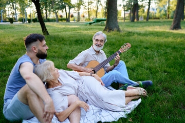 Senior Man Playing Guitar with Family Outdoors in a Green Park