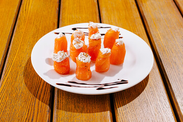 Colorful salmon rolls topped with cream cheese sit artfully on a white plate