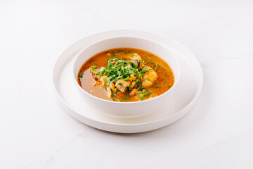 Delicious soup with fresh herbs served in a white bowl on a marble table