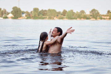 A joyful moment shared in the water: a dad and a child girl, both smiling, embrace playfully in a...