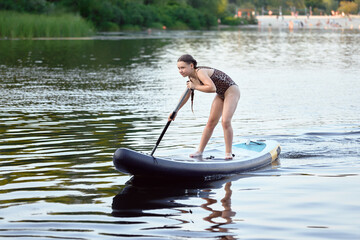 Teenage Girl Paddleboarding on a Calm Lake During a Sunny Day Outdoors