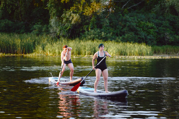 A man and woman enjoy a sunny day paddleboarding on a calm lake amidst lush vegetation. Perfect...