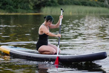 A woman with short hair practices paddling on a paddleboard while enjoying a calm lake setting with...