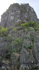 Steep limestone cliff covered with patches of green vegetation and rugged rock formations of Thien Cung Cave, Ha Long Bay, Vietnam.
