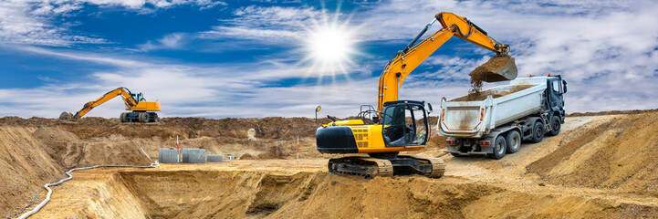 Ein Bagger arbeitet auf einer Baustelle und belädt einen LKW mit Erde aus einer Baugrube für...