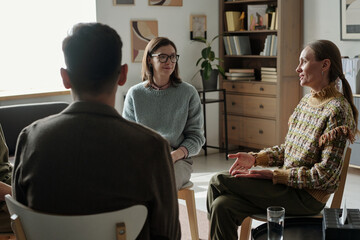Group of women and men sitting in therapy session, engaging in conversation, sharing experiences,...