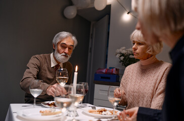 Group of three individuals enjoying a candlelit dinner together, engaging in conversation and sharing a quiet meal. Setting is cozy and emphasized by warm lighting and elegant dining arrangements.