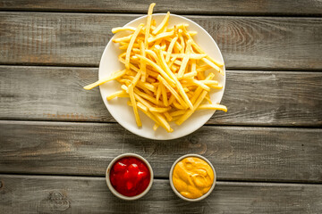 Potato chips on plate near sauces on dark wooden table top-down copy space