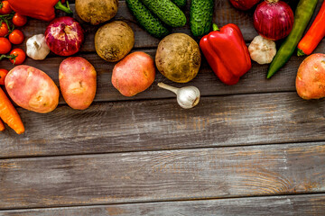 Set of autumn vegetables - potato, cucumber, carrot, greenery - on dark wooden background top-down...