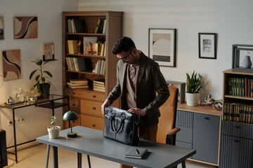 Man standing in office opening black briefcase on desk preparing for therapy session with...