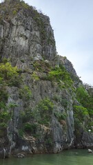 Steep limestone cliff covered with patches of green vegetation and rugged rock formations of Thien Cung Cave, Ha Long Bay, Vietnam.
