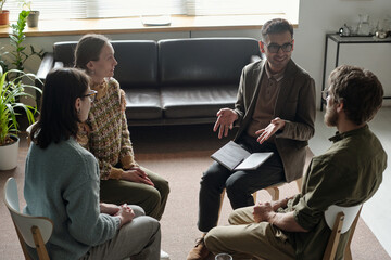 Man leading group therapy session with two women and man sitting in circle, participants listening...