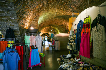 A colorful display of clothes and shoes lines the interior of a local market beneath a historic...