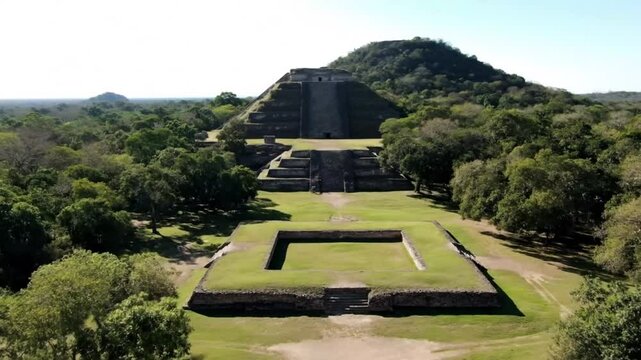 An aerial view captures the uxmal mayan pyramid rising majestically amidst lush green trees under a clear sky, showcasing ancient architecture