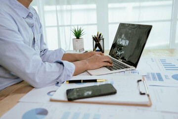 Asian businessman working at desk analyzing financial reports, charts and data using laptop to plan strategies, track performance and predict market trends for success.