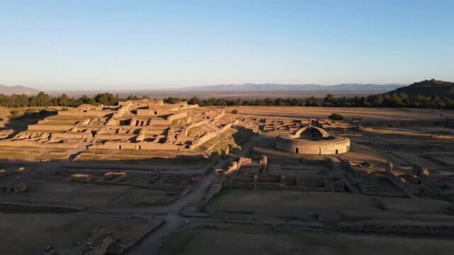 An aerial view captures the ancient ruins of a prehispanic city with stone structures and a circular building nestled in a vast, arid landscape