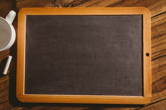 Fototapeta Flat design showing wood-framed chalkboard is lying on plank tabletop, with ceramic mug and chalk
