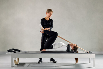 Instructor guiding a client in a pilates reformer stretch at a studio