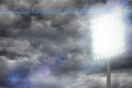 Flat design stadium floodlight tower shining through rain under overcast sky creating lens flares