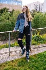 Smiling young woman wearing inline skates leaning on a fence in an urban park, enjoying a sunny...