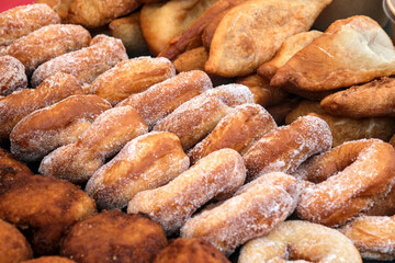 Assorted fried pastries and sugar-coated donuts stacked at a market stall, showcasing golden textures and delicious homemade treats.