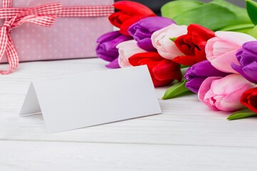 Displaying flat-design folded greeting card on white tabletop with colorful tulips and gift box