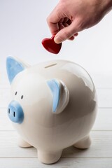 Hand putting heart shape coin in piggy bank