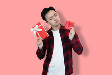 A young Asian man in a red plaid shirt and white t-shirt holds two red gift boxes, His facial...