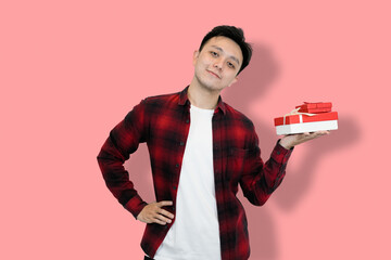 A young Asian man, wearing a red plaid shirt over a white t-shirt, is holding a red gift box
