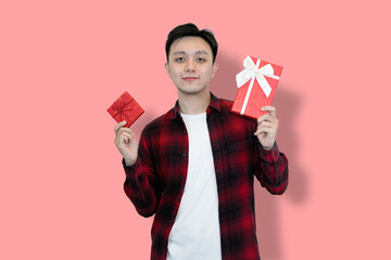 A young Asian man in a red plaid shirt and white t-shirt holds two red gift boxes, His facial...