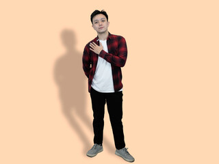 A young Asian man stands against a pale orange background, with one hand placed over his heart