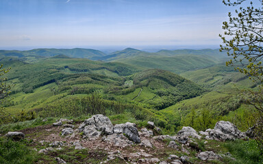 Obraz premium View of the forest-covered Bükk Mountains from Három-kő, framed by rocky outcrops and a wide valley below on a clear spring day.