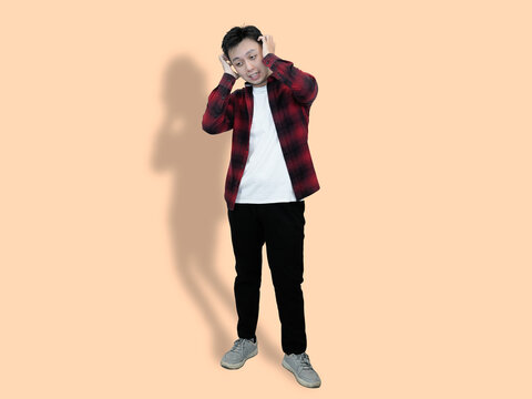 A young Asian man stands against a pale orange background, expressing frightened or scared
