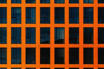 Modern office facade with orange cladding and dark blinds forming a repetitive geometric grid