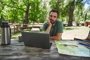 Man Outdoors Using Laptop Near Map and Gear on a Sunny Day