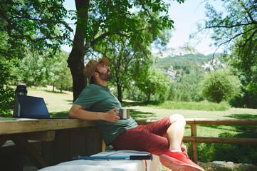 Outdoor Adventurer Relaxing in Scenic Nature with Coffee and Laptop