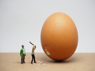 Mini toy of action figure at table with blurred background. Miniature photography concept design. Minifigure of worker hit the egg with hammer.