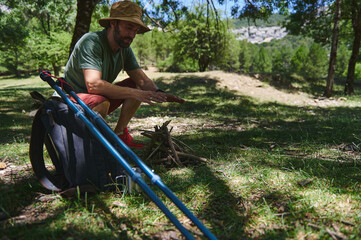 Man Preparing Bonfire in Forest Clearing with Backpack and Hiking Equipment
