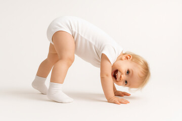 Joyful caucasian toddler in white onesie posing playfully on all fours in studio. The child smiles brightly while standing bent over, hands and feet on the floor.