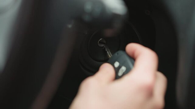 Close up of road traveler inserting metal key into ignition starter and turning key inside vehicle cabin focusing on hand movement dashboard detail and winter jacket sleeve before engine start