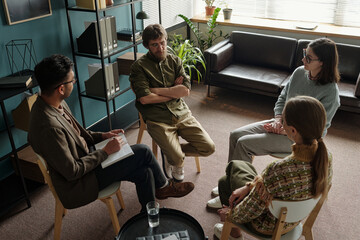 Group of multiethnic men and women sitting in therapy session, therapist holding notepad and...
