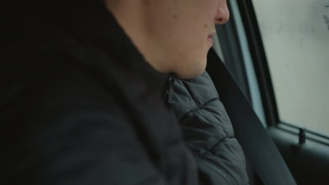 Close up of road traveler putting on car seat belt while sitting beside fogged window wearing winter jacket focusing on hand movement safety preparation during commute